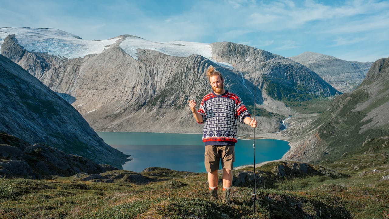 Bearded man in traditional sweater holding fishing rod in Nordland, Norway, with stunning glacier background.